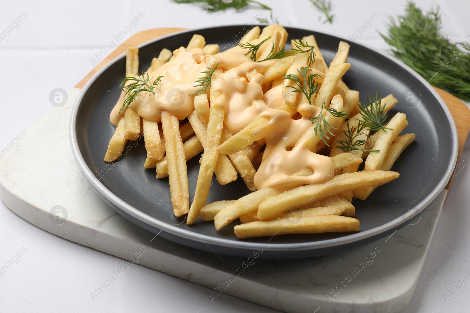 Photo of Delicious french fries with cheese sauce and dill on white table, closeup