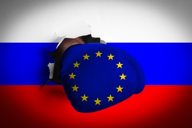 Image of Man in boxing glove with European union stars punching hole through Russian flag, closeup. Political feud