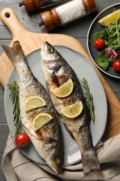 Delicious baked fish served on grey wooden table, top view