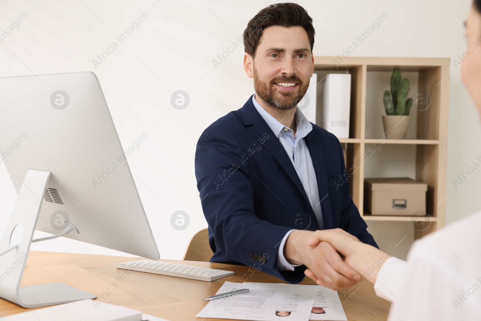 Photo of Human resources manager shaking hands with applicant during job interview in office