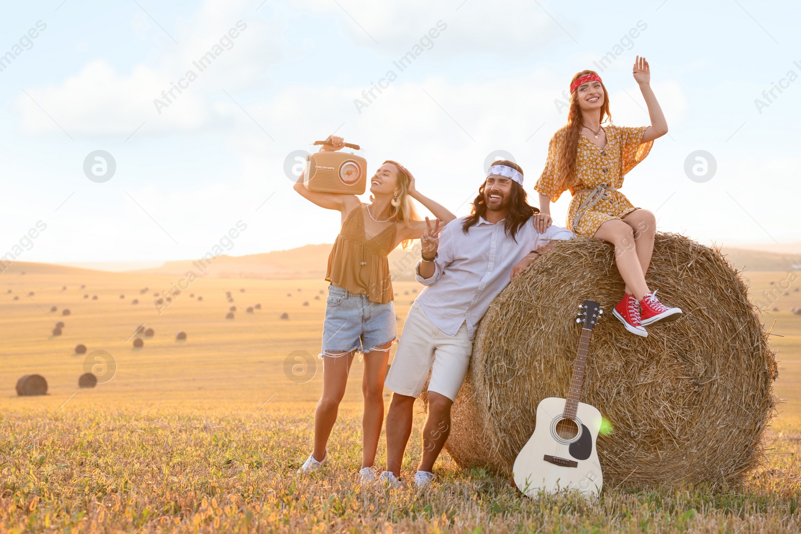 Photo of Happy hippie friends with radio receiver and guitar in field, space for text