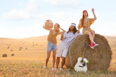 Photo of Happy hippie friends with radio receiver and guitar in field, space for text
