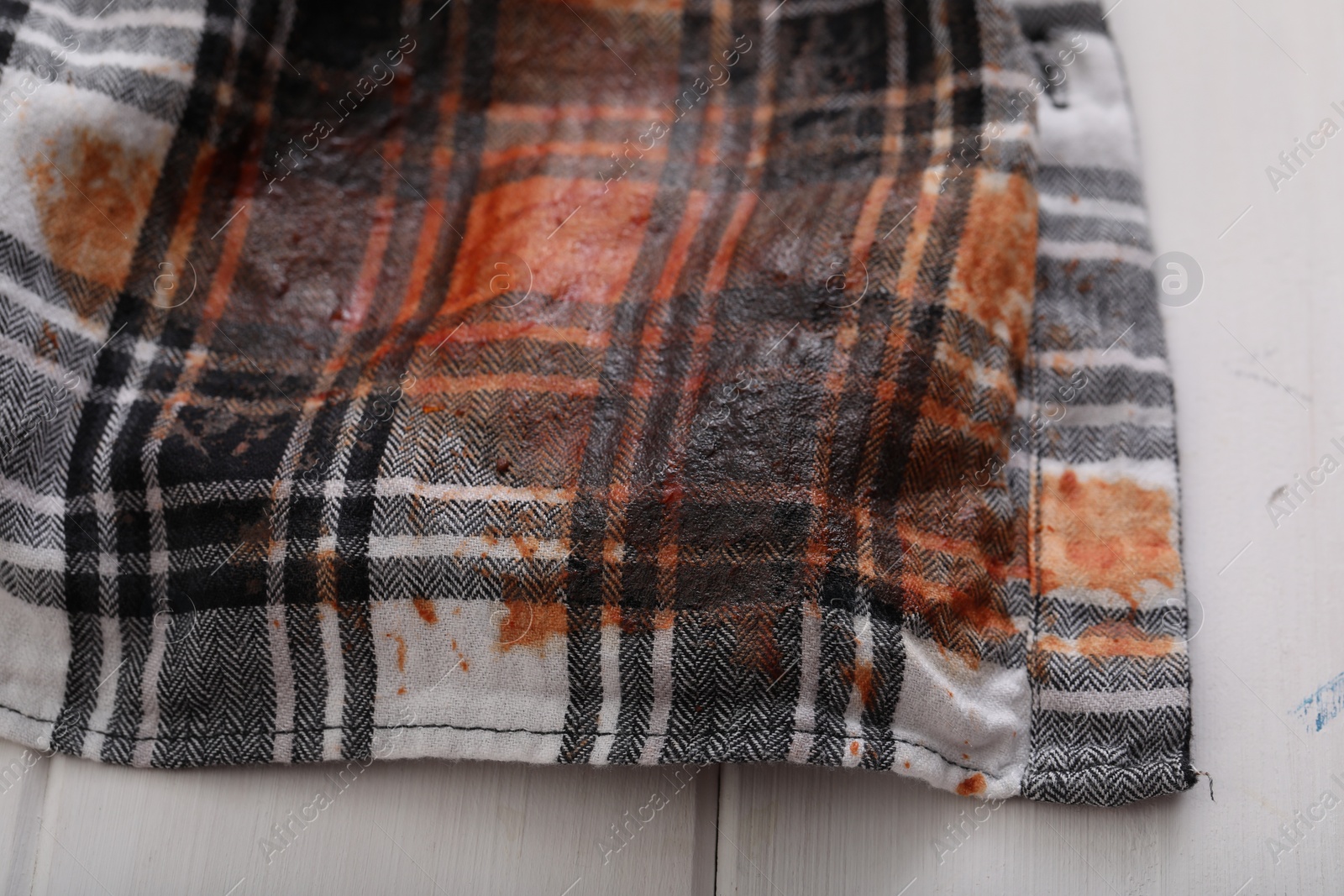 Photo of Shirt with stain of sauce on white wooden table, closeup