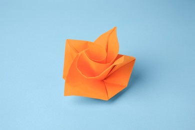 Photo of Origami art. Handmade orange paper flower on light blue background