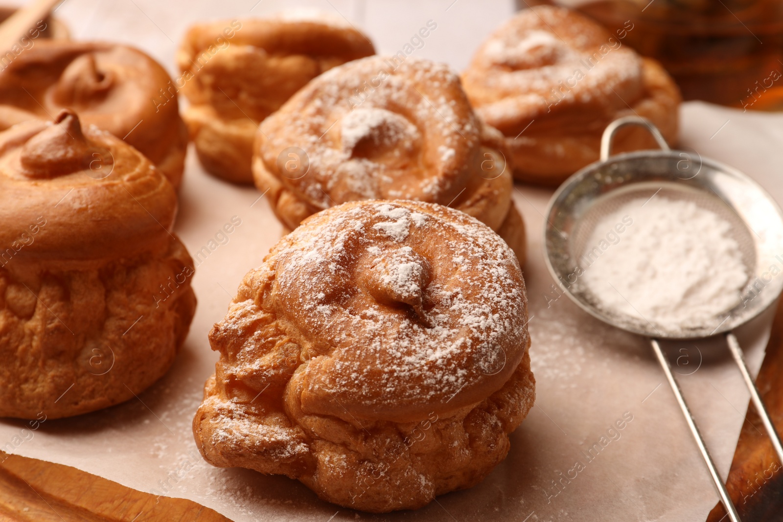 Photo of Delicious profiteroles with powdered sugar on wooden board, closeup