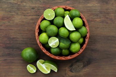 Photo of Whole and cut fresh ripe limes in bowl on wooden table, flat lay