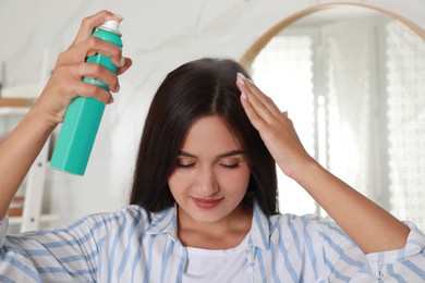 Photo of Woman applying dry shampoo onto her hair near mirror indoors