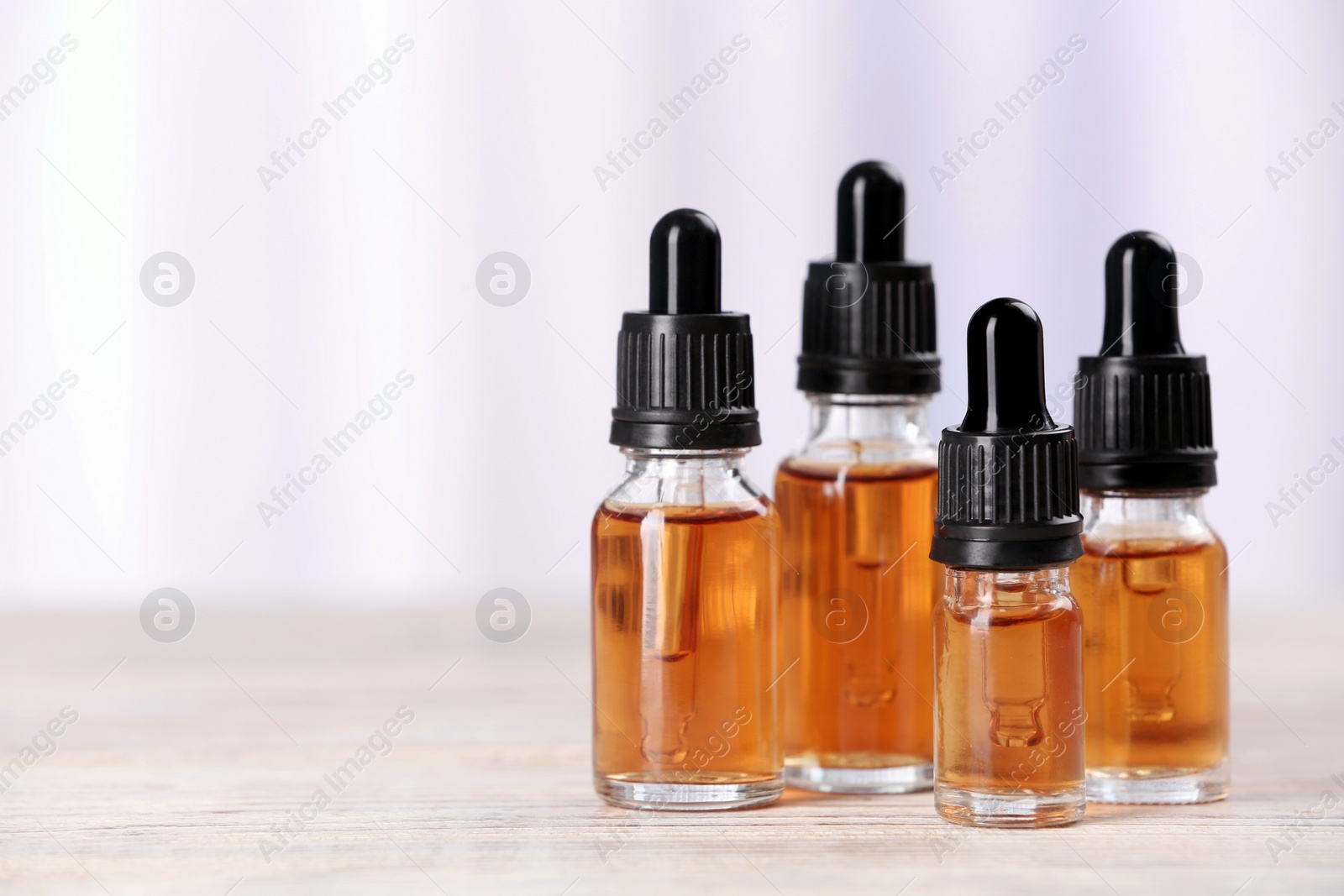 Photo of Bottles of essential oils on table against light background, space for text. Cosmetic products