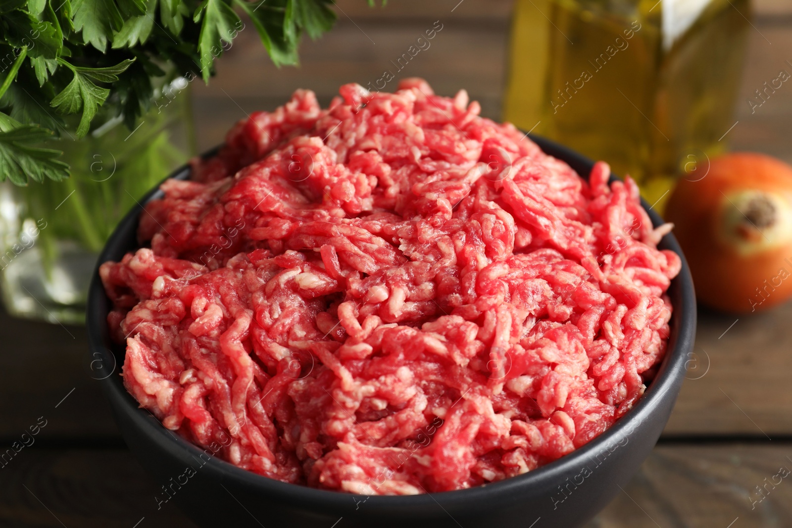 Photo of Raw ground meat in bowl and parsley on wooden table, closeup