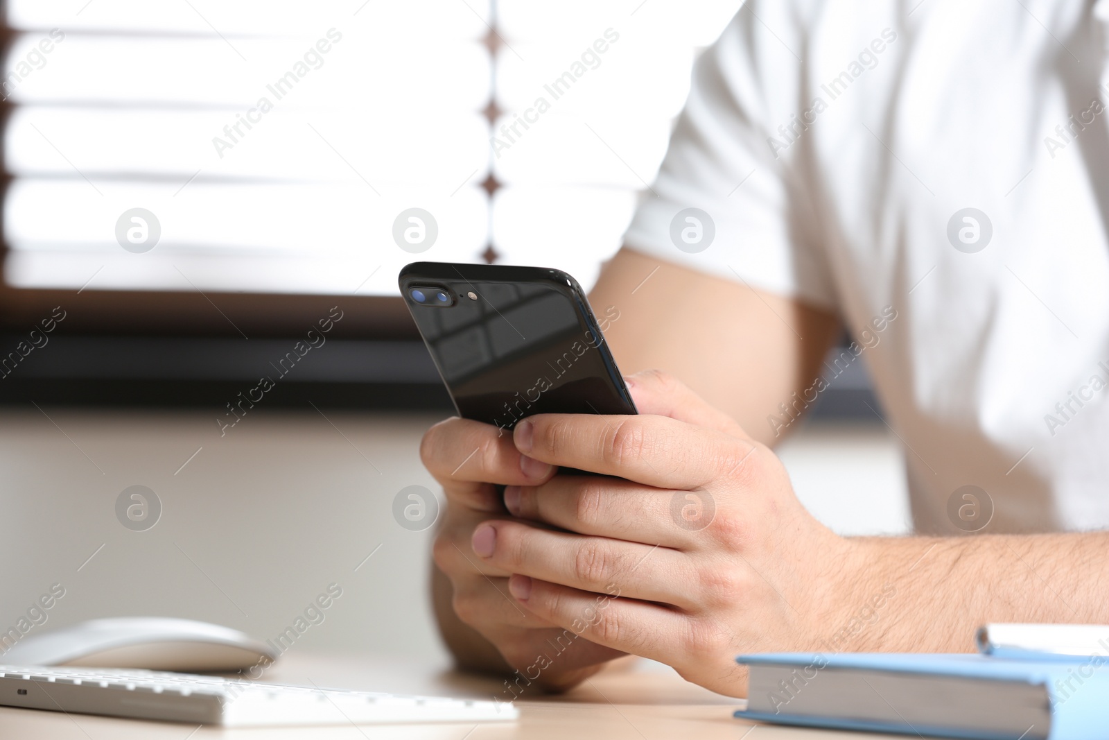 Photo of Young man using smartphone at table indoors, closeup