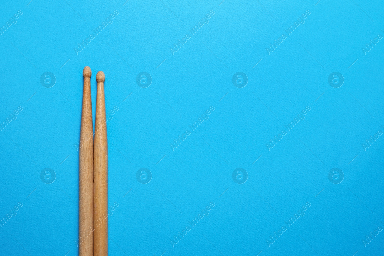 Photo of Two wooden drum sticks on light blue background, top view. Space for text