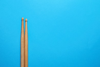 Two wooden drum sticks on light blue background, top view. Space for text