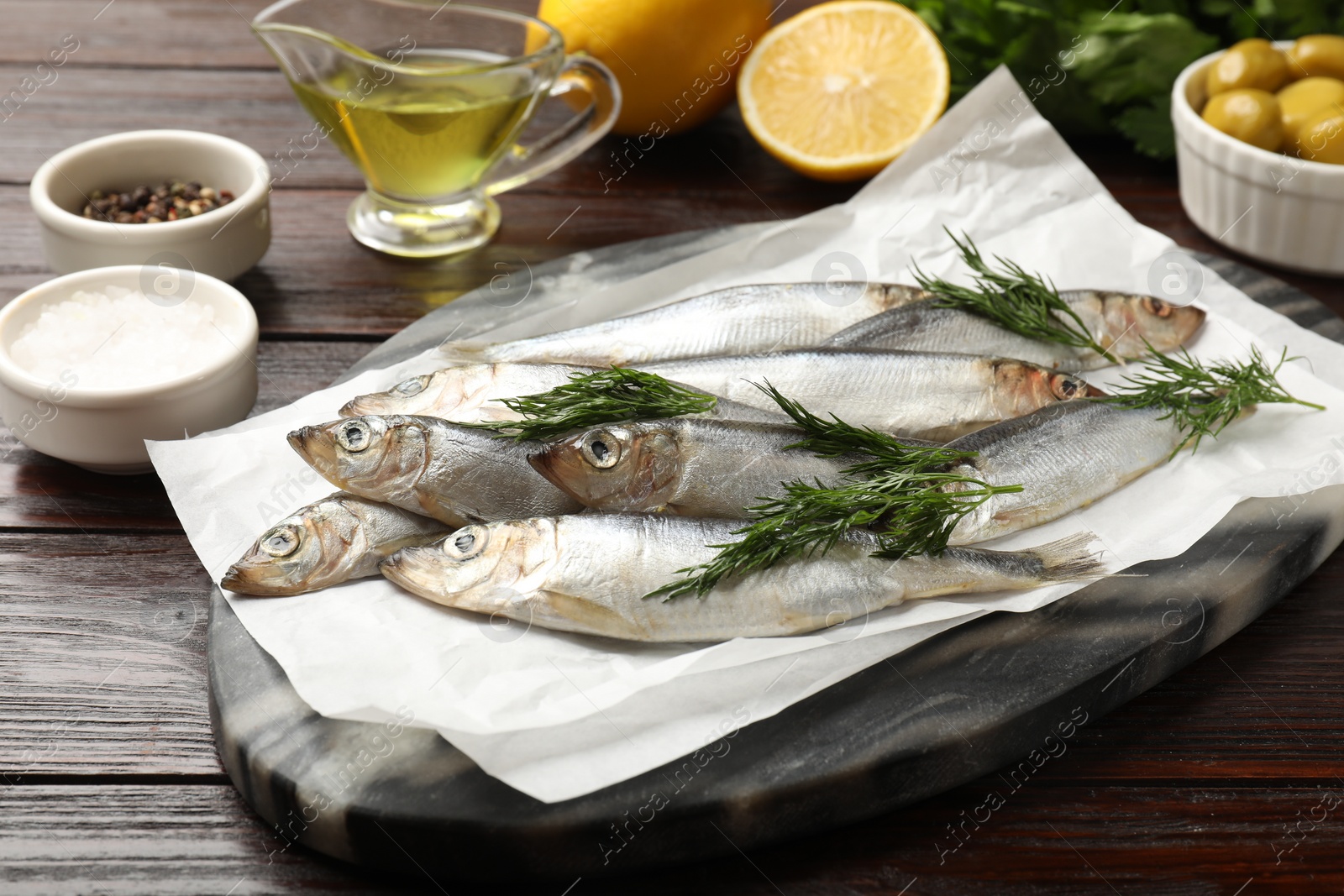 Photo of Fresh raw sprats, dill and other products on wooden table, closeup