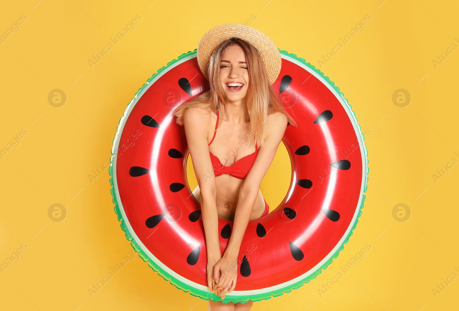 Photo of Beautiful young woman in stylish bikini with watermelon inflatable ring on yellow background