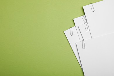 Photo of Sheets of paper with clips on light green background, top view. Space for text