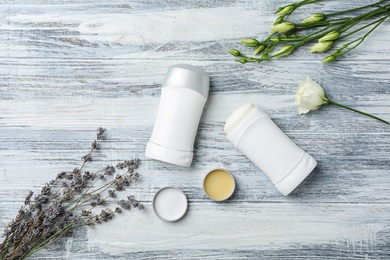 Photo of Flat lay composition with different deodorants and flowers on wooden background