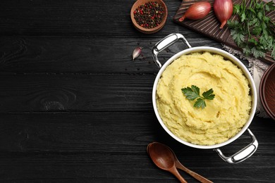 Pot of tasty mashed potatoes with parsley on black wooden table, flat lay. Space for text