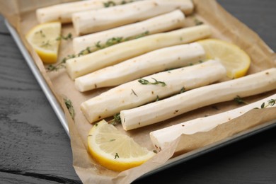 Photo of Baking tray with raw salsify roots, lemon and thyme on grey wooden table, closeup