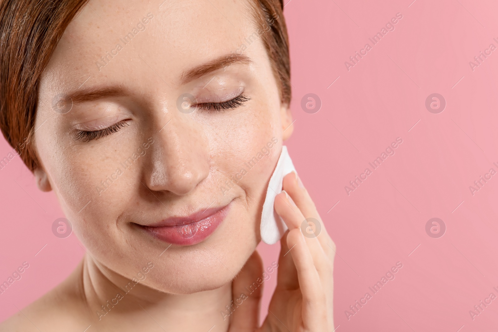 Photo of Beautiful woman with freckles wiping face on pink background, closeup. Space for text