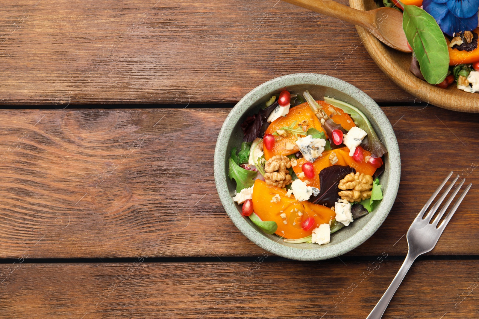 Photo of Delicious persimmon salad with cheese and pomegranate served on wooden table, flat lay. Space for text