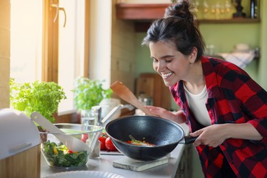 Photo of Young woman holding pan with freshly fried eggs and vegetables in kitchen