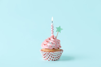 Birthday cupcake with burning candle and topper on light blue background