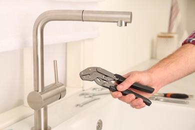 Photo of Man with wrench near sink in kitchen, closeup. Water tap installation