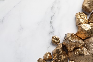 Photo of Pile of shiny gold nuggets on white marble table, flat lay. Space for text