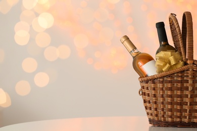 Photo of Wicker basket with bottles of wine against blurred lights. Space for text