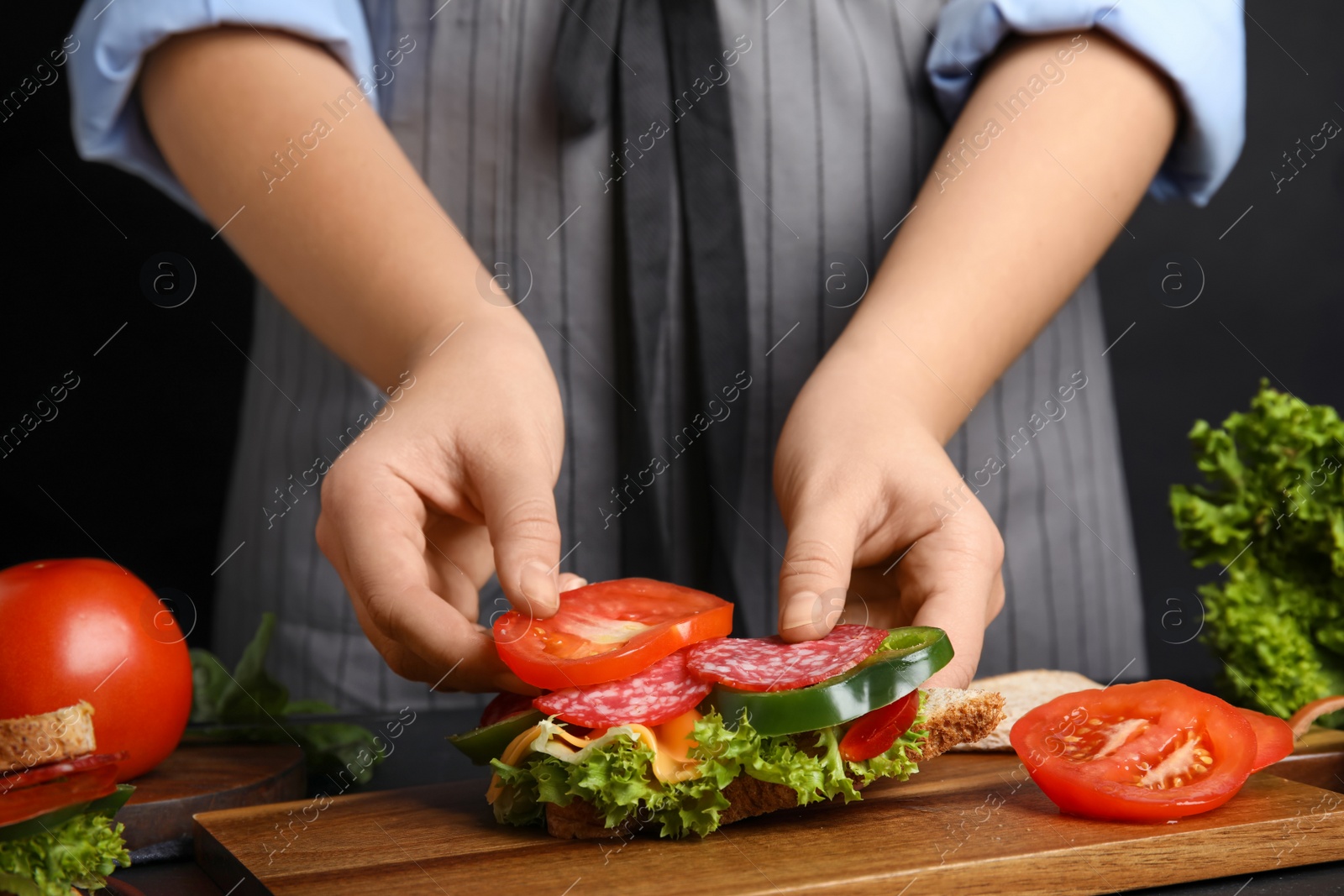 Photo of Woman adding tomato to sandwich at table, closeup