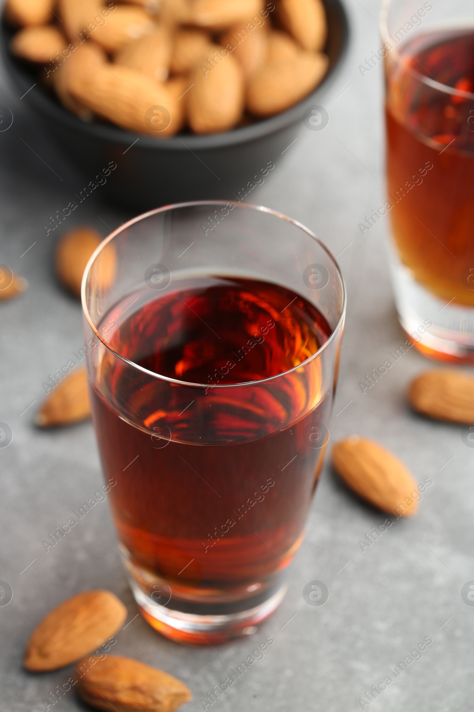 Photo of Glass with tasty amaretto liqueur and almonds on gray table, closeup