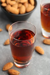 Glass with tasty amaretto liqueur and almonds on gray table, closeup