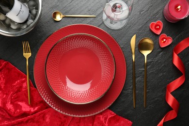 Romantic place setting with candles and red ribbon on dark gray textured table, flat lay