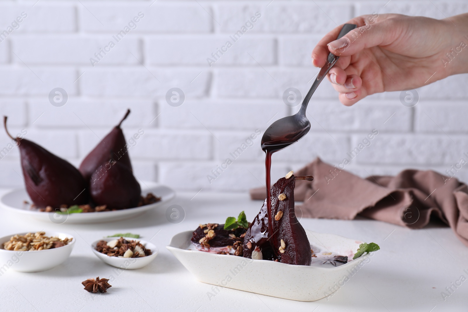 Photo of Woman pouring red wine on tasty poached pears in bowl at white table, closeup