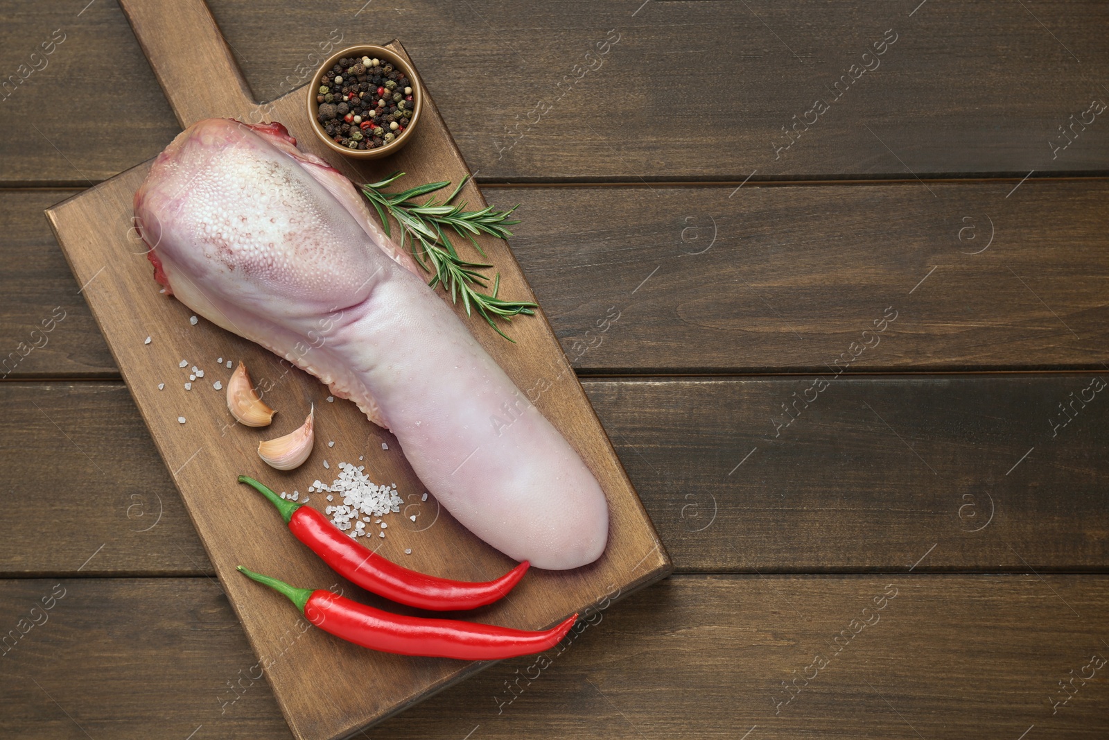 Photo of Raw beef tongue, peppercorns, garlic, salt, rosemary and chili peppers on wooden table, top view. Space for text