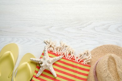 Photo of Beach towel, hat and flip flops on white wooden background, flat lay. Space for text