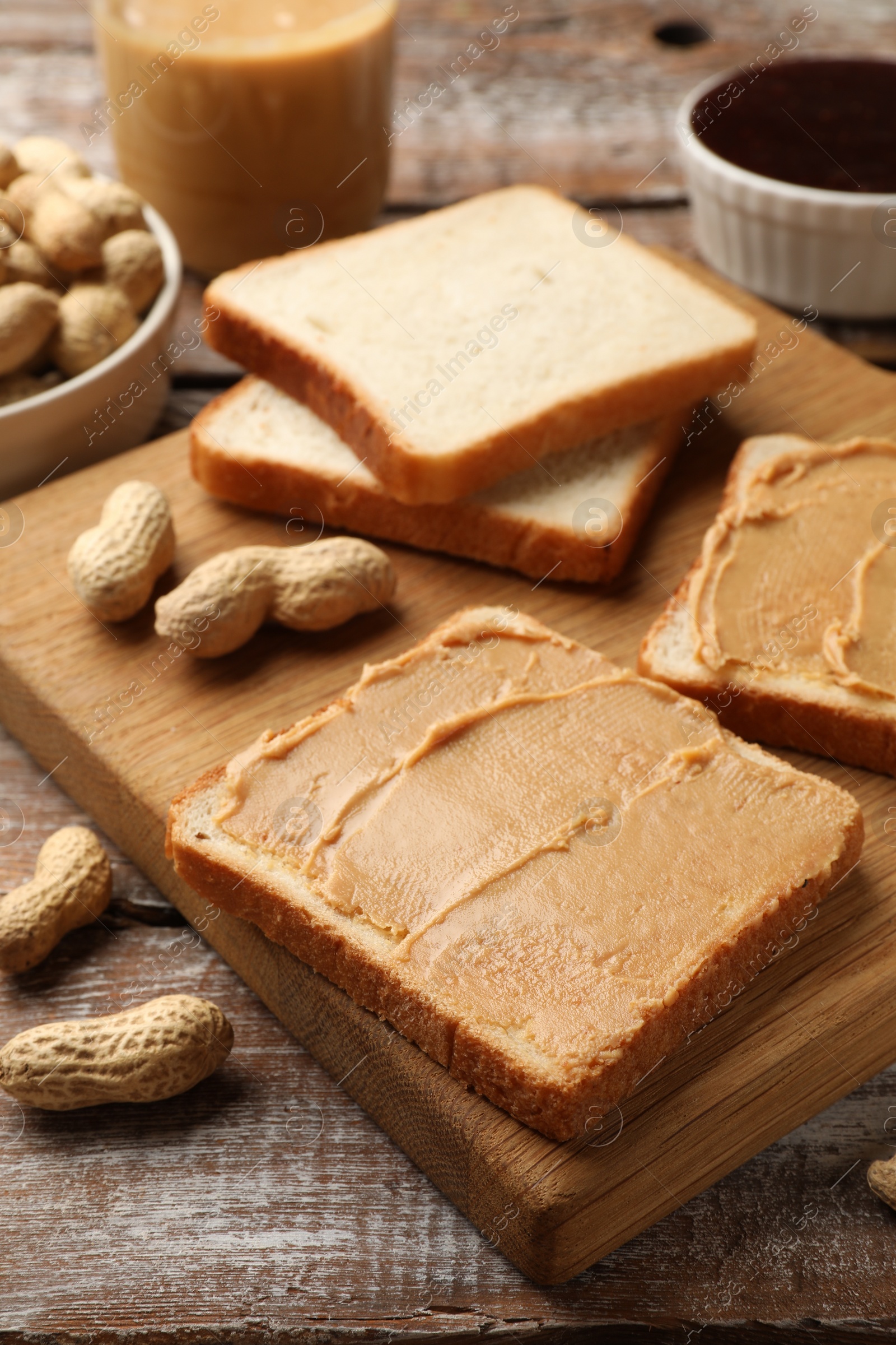 Photo of Tasty peanut butter sandwiches and peanuts on wooden table, closeup