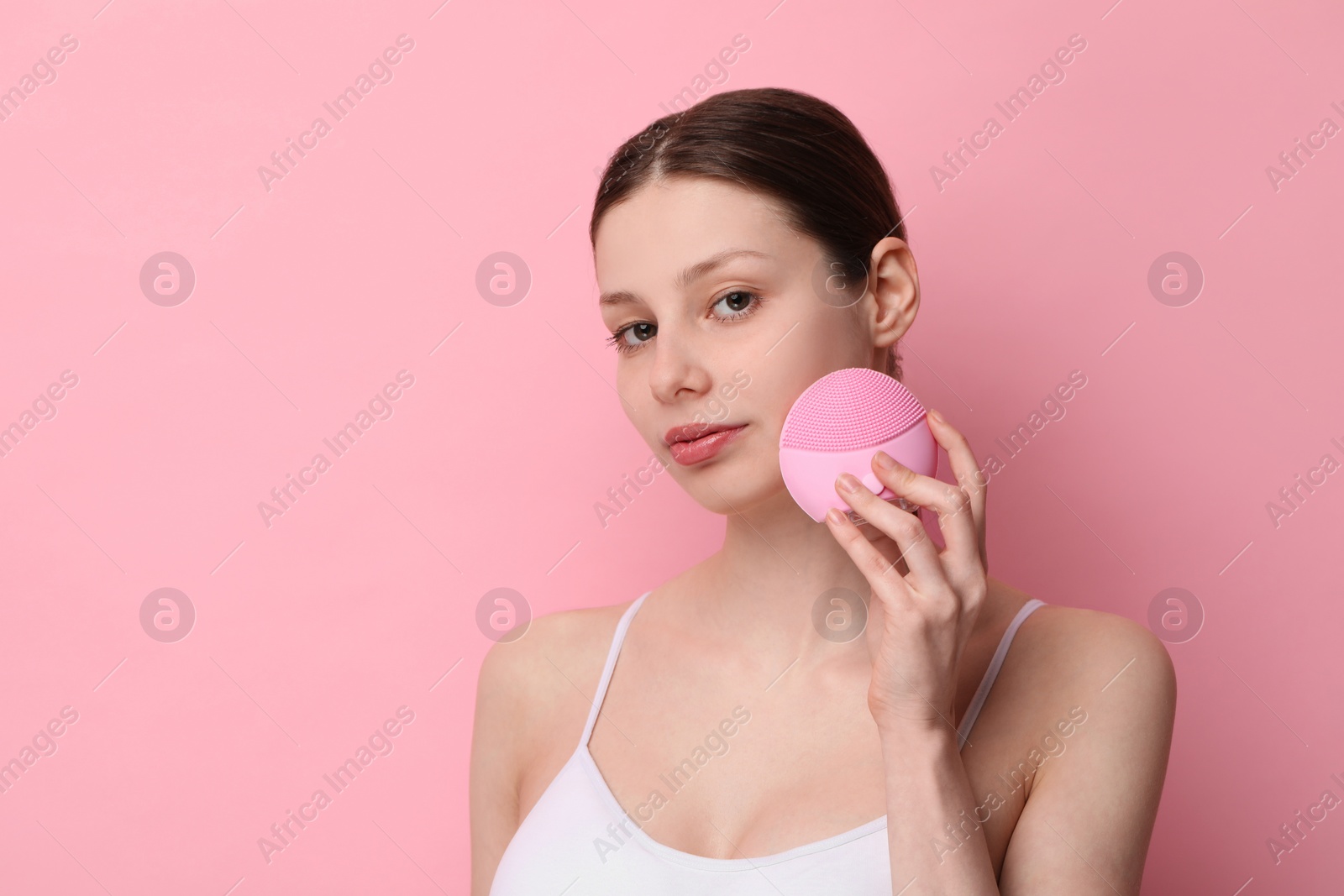 Photo of Washing face. Young woman with cleansing brush on pink background, space for text