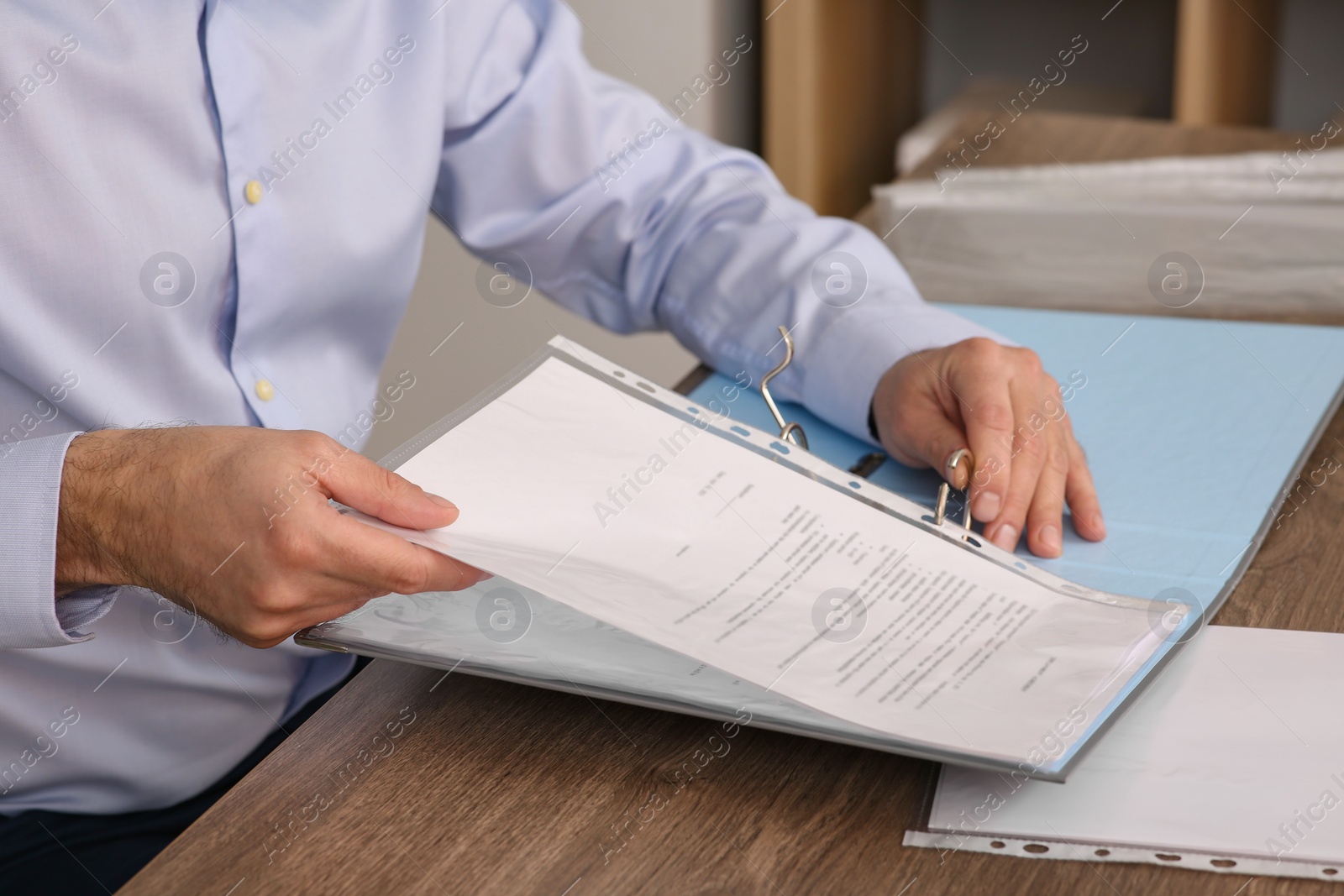 Photo of Businessman putting document into file folder at wooden table in office, closeup