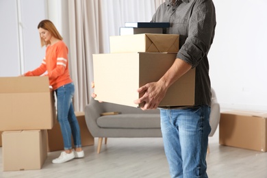 Photo of Man carrying moving boxes while woman unpacking other in new house