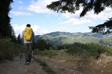 Photo of Tourist with backpack and trekking poles hiking through mountains, back view. Space for text