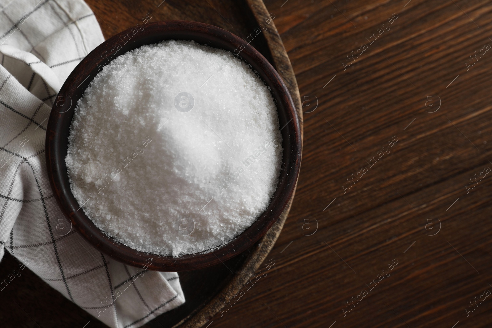 Photo of Organic salt in bowl on wooden table, top view. Space for text