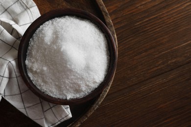 Photo of Organic salt in bowl on wooden table, top view. Space for text