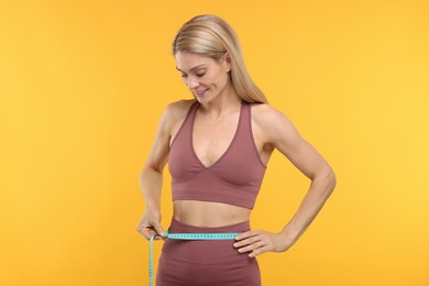 Photo of Slim woman measuring waist with tape on yellow background. Weight loss
