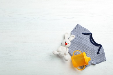 Flat lay composition with bodysuit and space for text on white wooden background. Baby accessories