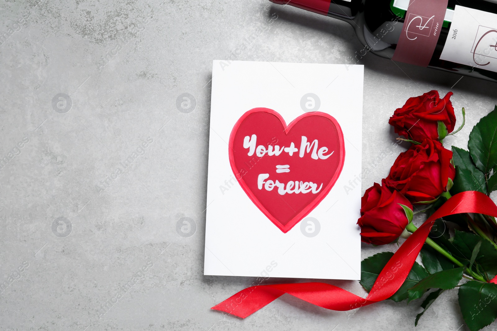 Photo of Marvelous message of love with red roses and wine on grey table, flat lay. Space for text