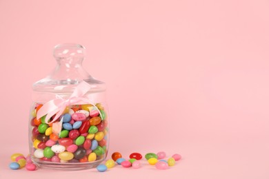Photo of Glass jar with different candies on pink background, space for text