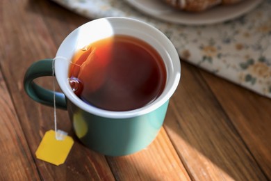 Photo of Tea bag in cup on wooden table, closeup
