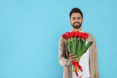 Photo of Happy man with red tulip bouquet on light blue background, space for text. 8th of March celebration