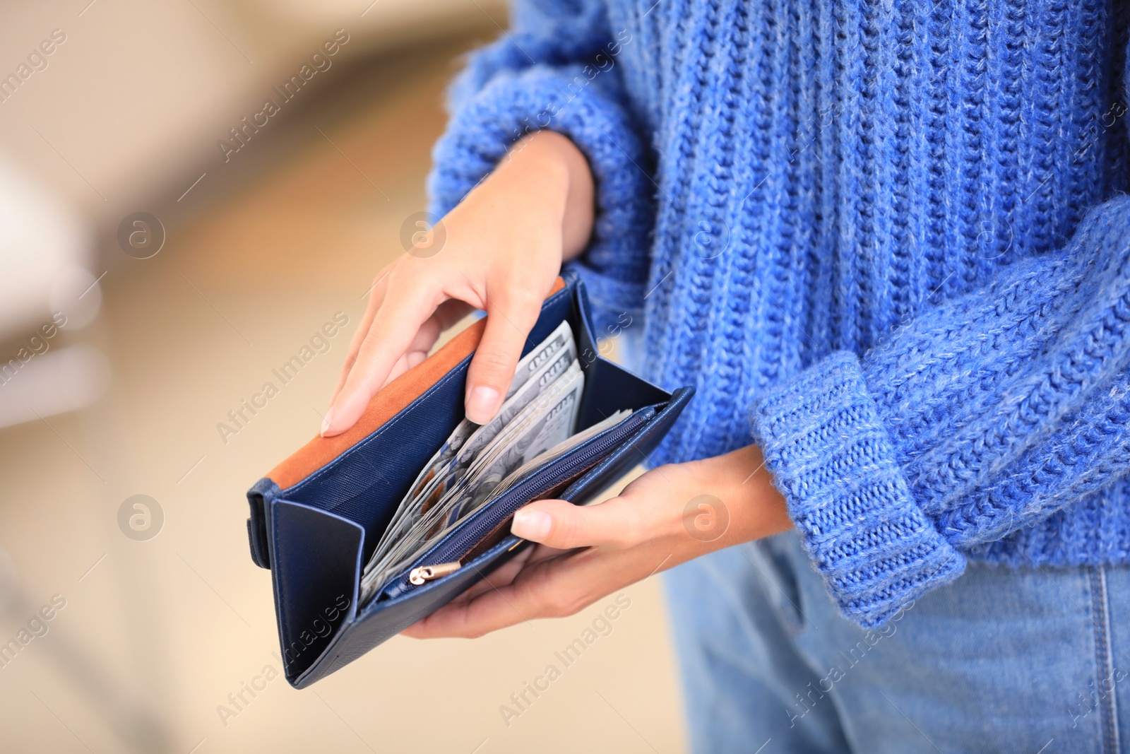 Photo of Young woman holding wallet with dollar bills on blurred background, closeup